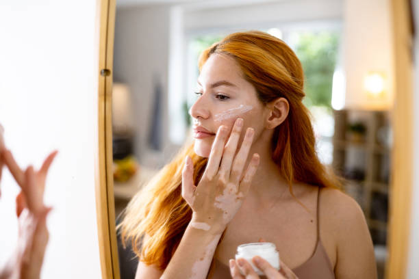 Red-haired woman applying face cream while looking in mirror