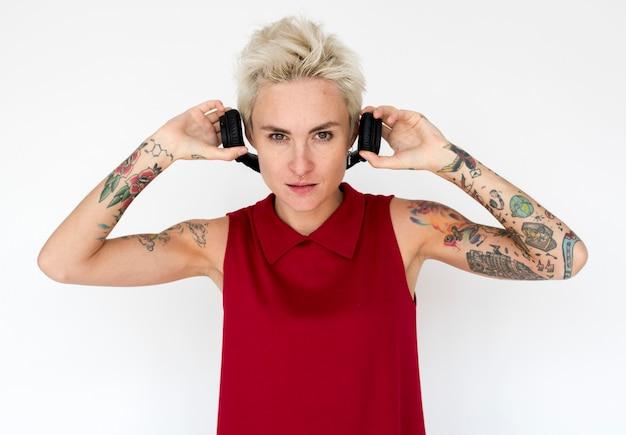 Woman with blonde hair and tattoos wearing red sleeveless top holding headphones