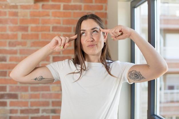 Woman thinking with fingers on temples indoors with brick wall background