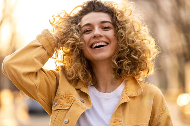 Happy young woman with curly hair wearing a yellow jacket outdoors